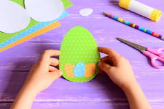 小孩子手里拿着复活节纸卡.孩子们制作了有创意的彩蛋形复活节贺卡.在木制桌子上进行艺术活动的材料.幼稚园或家中手工造纸工艺概念