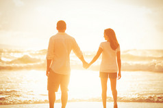 在日落时在沙滩上散步的情侣