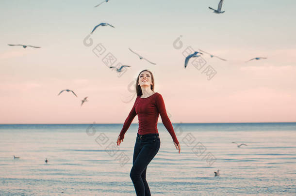 肖像的幸福的微笑笑兴奋高加索运行跳海鸥鸟<strong>群</strong>当中日秋高气爽的秋季户外在岸滩上在日落，生活方式自然情感的牛仔裤的年轻女子