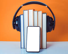 有声读物概念。耳机在橙色和白色背景上放上书。智能手机。手机.