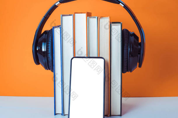 有声读物概念。耳机在橙色和白色背景上放上书。智能手机。手机.