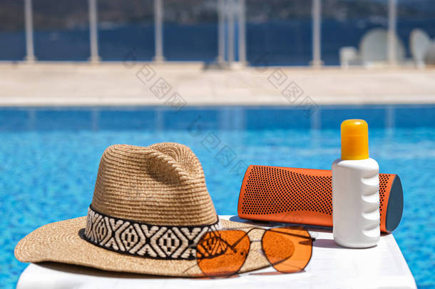 游<strong>泳池</strong>附近的橙色海滩饰物。<strong>防晒霜</strong>、太阳镜、音乐扬声器和草帽