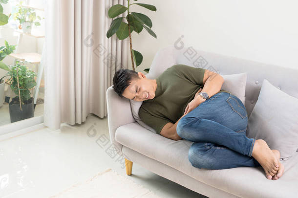 <strong>男人</strong>从剧烈的疼痛中挣扎着抓住肚子，躺在沙发上