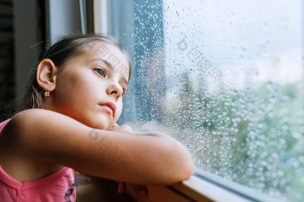 小女孩忧心忡忡地望着窗玻璃里的雨滴很多。悲伤童年的概念形象.