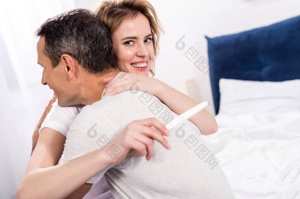 愉快的夫妇与怀孕测试互相拥抱在家