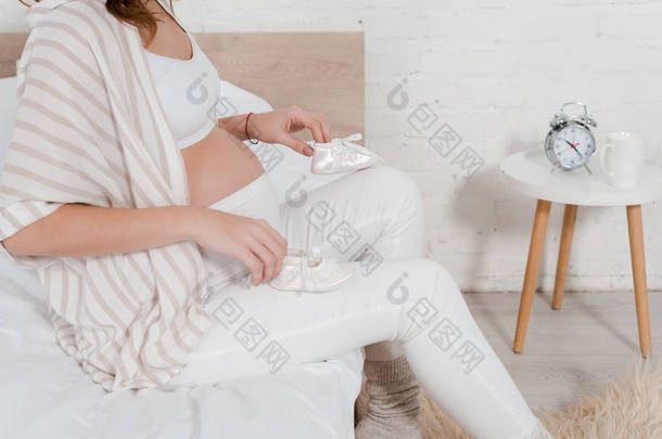 孕妇躺<strong>在</strong>床上抱着婴儿靴的剪影 