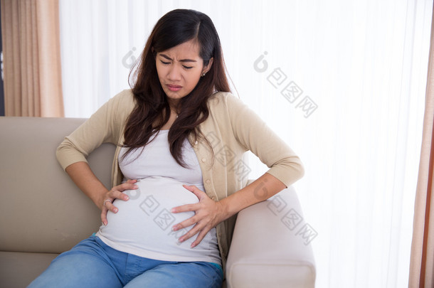 Asian pregnant woman has stomachache sitting on her couch