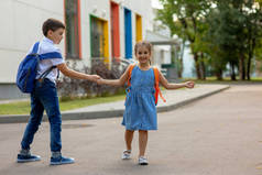 一个笑容满面的小女孩和一个背着背包的弟弟手牵着手，玩耍着，在教学楼附近玩得很开心
