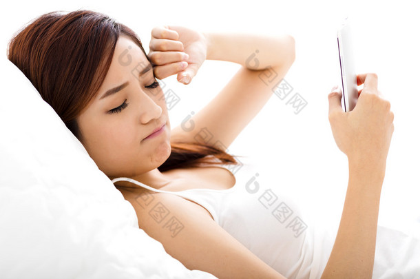 年轻的女人在床上用疲惫的眼神看智能手机