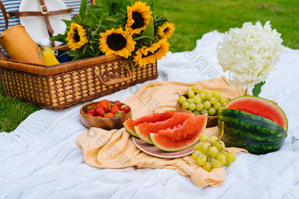 <strong>夏日</strong>野餐的概念,阳光灿烂,有西瓜、水果、花束、水仙花和向日葵花.带着食物的野餐篮和白色针织毛毯的令人神清气爽的夏季饮料。有选择的重点