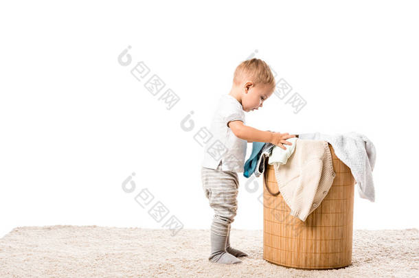 幼儿男孩站在柳条洗衣篮前的地毯上隔离在白色