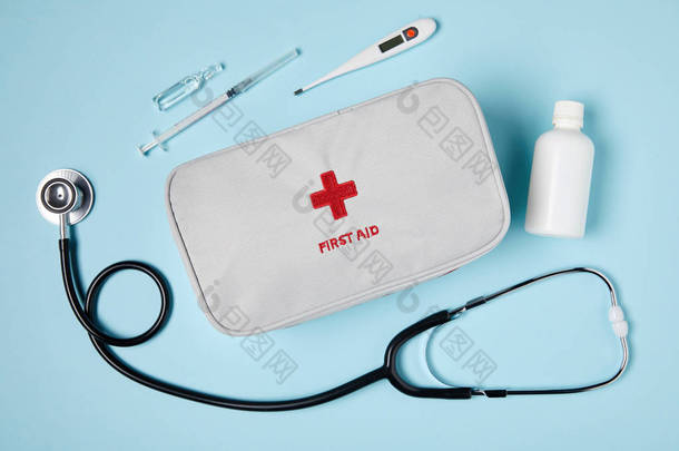 白色急救包袋与听诊器和药物在蓝色表面的顶部视图