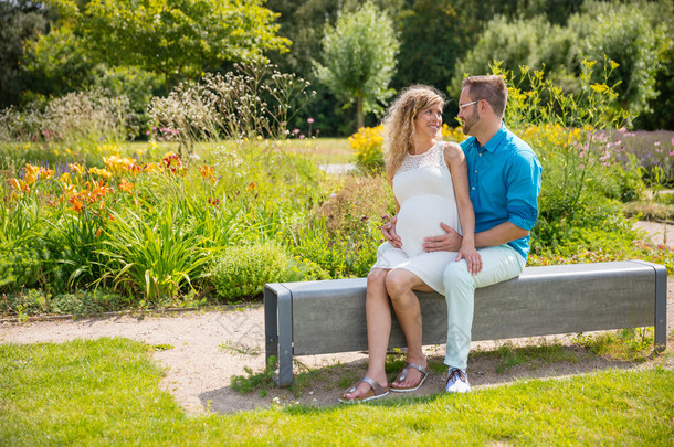 对幸福的夫妇怀孕了，坐在公园的长凳上
