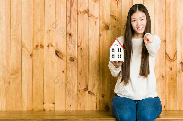 年轻的亚洲女人拿着一栋房子，像个笑脸，指着前面.