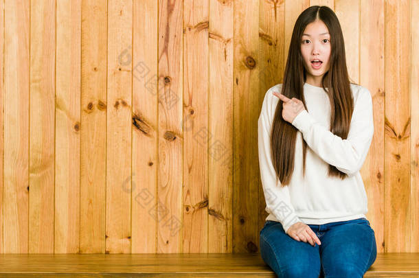 年轻的中国女人坐在一个指向侧边的木制地方