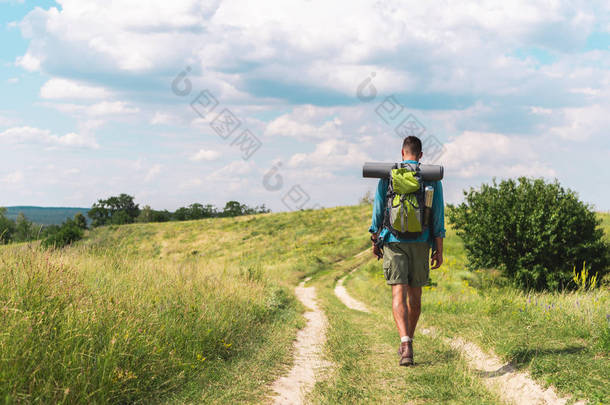 徒步旅行者与背包行走在绿色草地上的路径