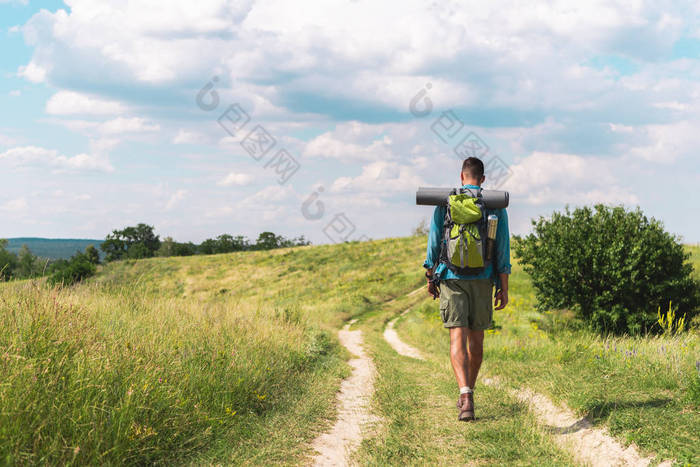 徒步旅行者与背包行走在绿色草地上的路径