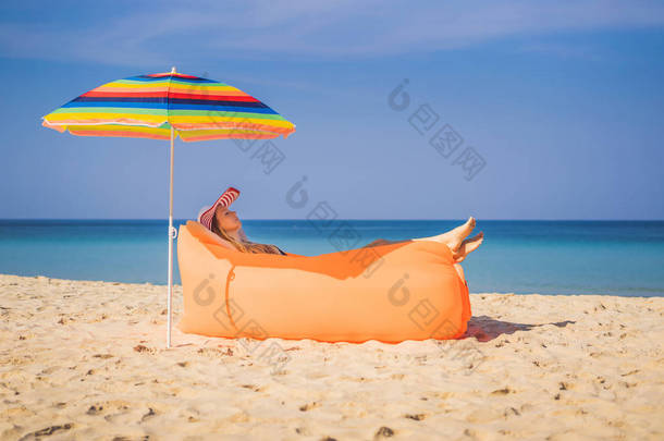 夏天生活方式的肖像漂亮的女孩坐在热带<strong>岛屿</strong>海滩上的橙色充气沙发上。在空气床上放松和享受生活