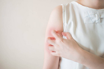 年轻妇女因在白色背景上发痒而抓挠胳膊。皮肤发痒的原因包括昆虫叮咬、皮炎、食物/药物过敏或皮肤干燥。卫生保健概念。靠近点.图片
