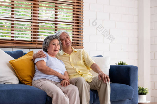 亚洲夫妇高级拥抱和<strong>舒适</strong>地坐在坐在一个房间里看电视.