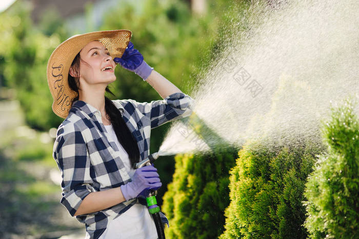 美丽的年轻园丁妇女浇水花园在炎热的夏天