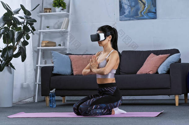 身穿运动服，头戴耳机的年轻女子坐在健身垫上在家锻炼