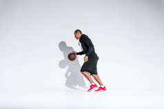 年轻的非洲裔美国运动员在灰色的篮球球上玩的全长视图 