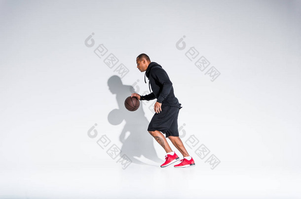 年轻的非洲裔美国运动员在灰色的<strong>篮球</strong>球上玩的全长视图 