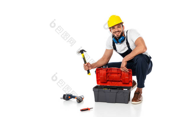 在工具箱和白色背景的工具旁边，穿着制服、手持铁锤的工人<strong>微笑</strong>