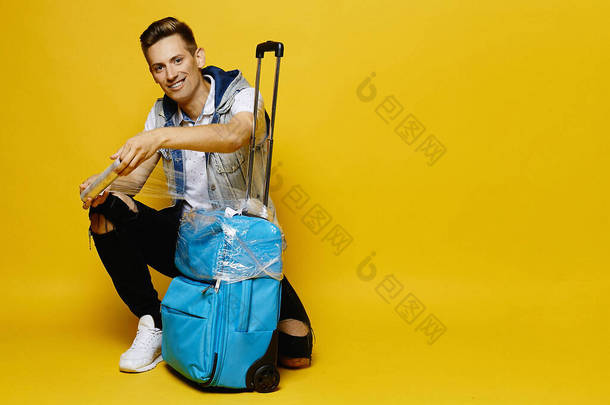 一个穿着斜纹棉布衣服的年轻人正在准备把他的旅行箱放进行李箱里，这个行李箱被黄色的背景隔开了。旅游广告的调侃