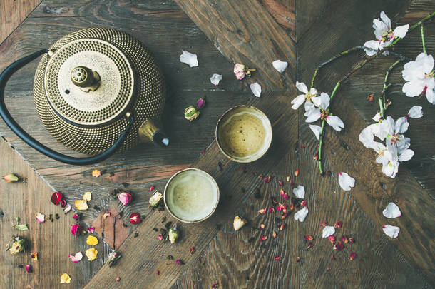 传统的亚洲茶道安排。铁茶壶, 杯子, 干玫瑰花蕾和盛开的杏仁树花在木桌背景上