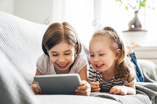 可爱的小孩在玩平板电脑.快乐的女孩在家里。可爱的妹妹们在孩子们的<strong>房间</strong>里玩得很开心. 