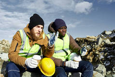 两名工业工人的肖像穿着反光夹克, 其中一个非洲人, 放松从工作中抽出咖啡休息和聊天在露天采矿工地