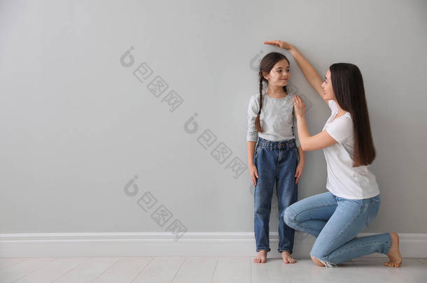 妈妈测量小女孩的身高接近室内浅灰的墙.案文的篇幅