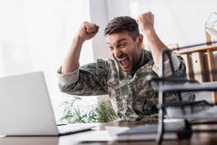 兴奋的军人在笔记本电脑和文件盘旁边欢欣鼓舞，前景朦胧