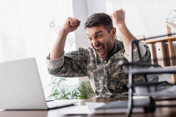 兴奋的军人在笔记本电脑和文件盘旁边欢欣鼓舞，前景朦胧