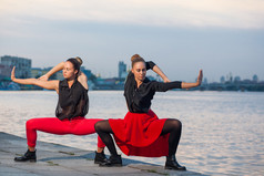 两个年轻漂亮的双胞胎姐妹在河附近的城市背景中起舞，waacking 舞蹈.