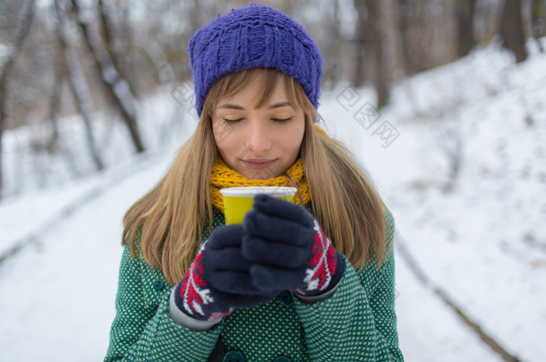 在绿色的上衣，拿着一杯很热的咖啡，与蒸汽与牛奶的女孩。孤独的女子站在白雪皑皑的冬天，空无一人上街头在公园里.