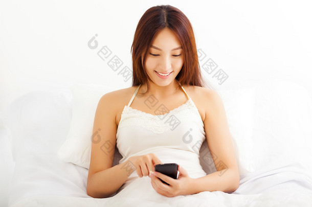 年轻的亚洲女人，躺在床上使用她的智能手机在她 bedr