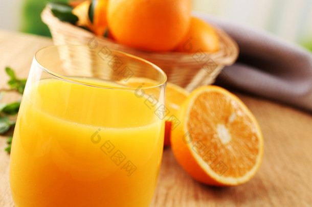Glass 橙果汁和柳条篮子与橘子在木桌和明亮的背景上