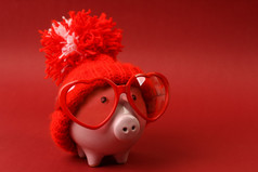 储钱罐顶红色的帽子与彩球站在红色的背景上红色的心形太阳镜爱上