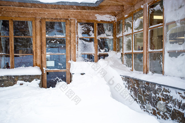 大窗户被在 snowst 的雪覆盖着奥地利座木头房子里