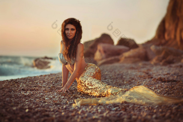美丽的幻想女人长长的金色礼服和贝壳花环.