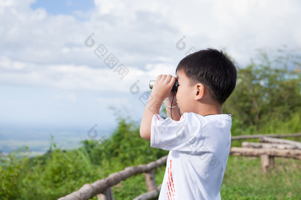 小的孩子看在双筒望远镜户外在阳光灿烂的夏天的一天 