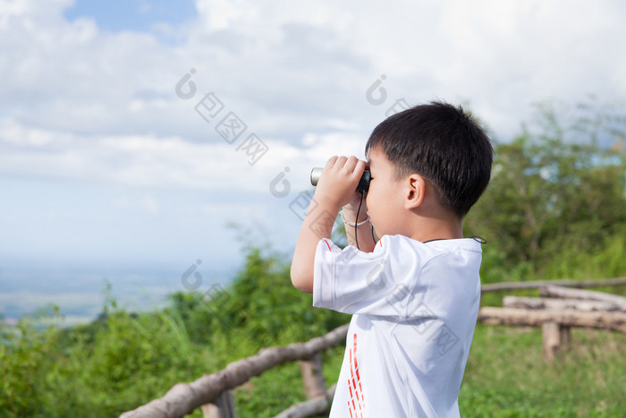 小的孩子看在双筒望远镜户外在阳光灿烂的夏天的一天 