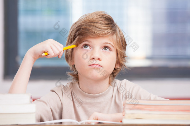 小学男孩在教室的课桌上，试图寻找新的想法