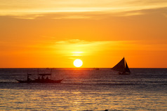 在日落时在热带海洋上的帆船。剪影照片.