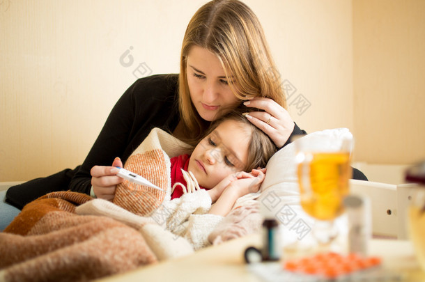 检查温度生病的女儿躺在床上的母亲