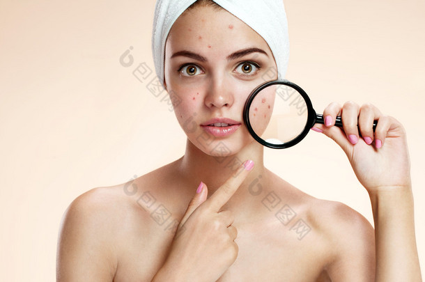 <strong>十</strong>几<strong>岁</strong>的女孩与问题皮肤用放大镜看疙瘩。女人的皮肤护理概念