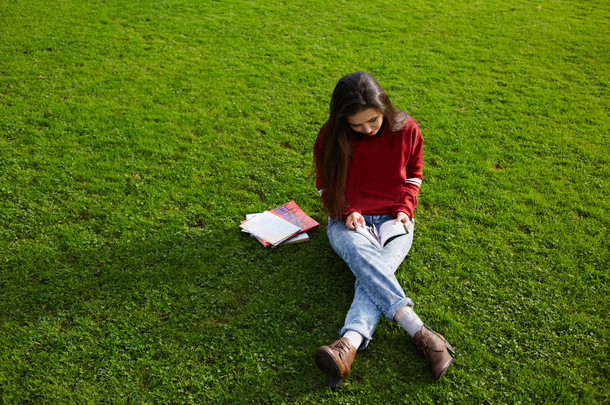 女孩坐在读一本书的草地上